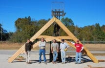 Five people with large wooden structure outdoors.